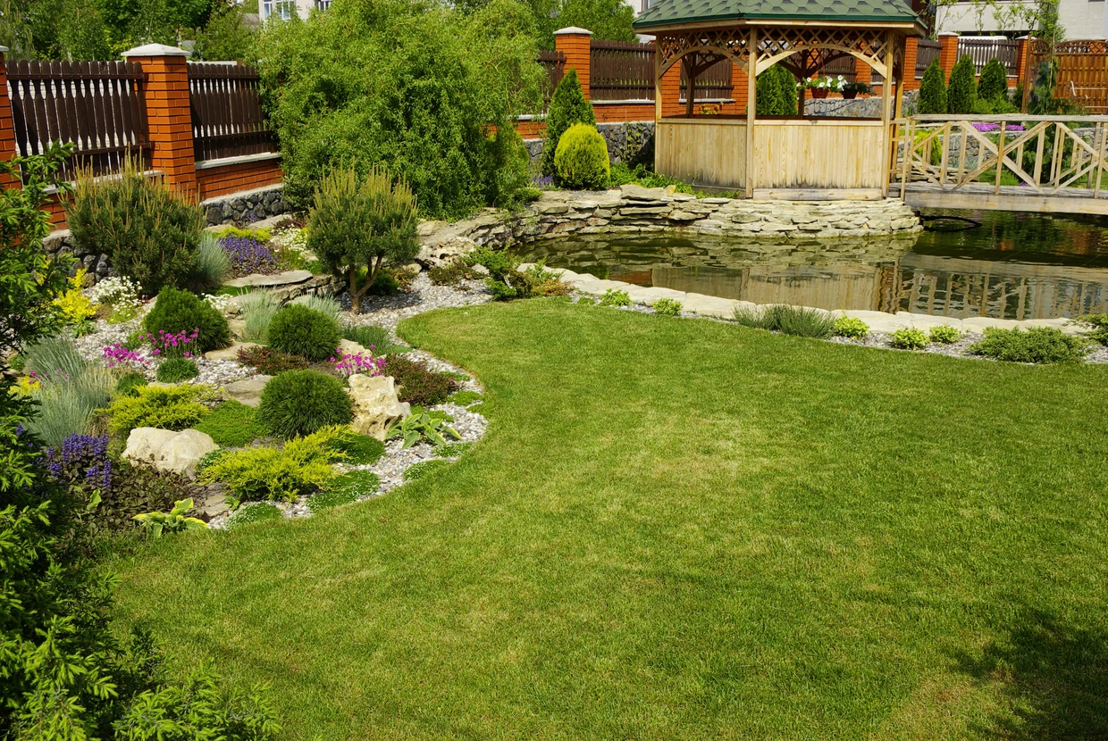 Jardin paysager avec pelouse centrale entourée de massifs rocheux et plantations variées