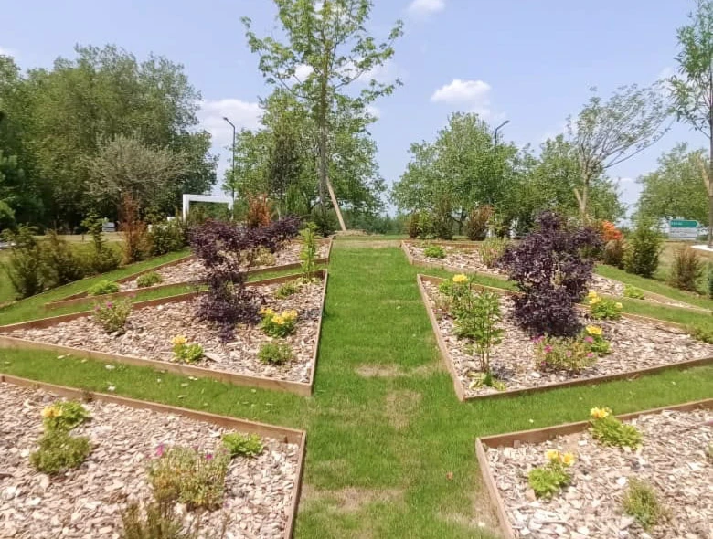 Jardin résidentiel avec terrasse en dalles béton jointoyées enherbées, mobilier d'extérieur composé d'une table ronde et chaises noires avec coussin rouge