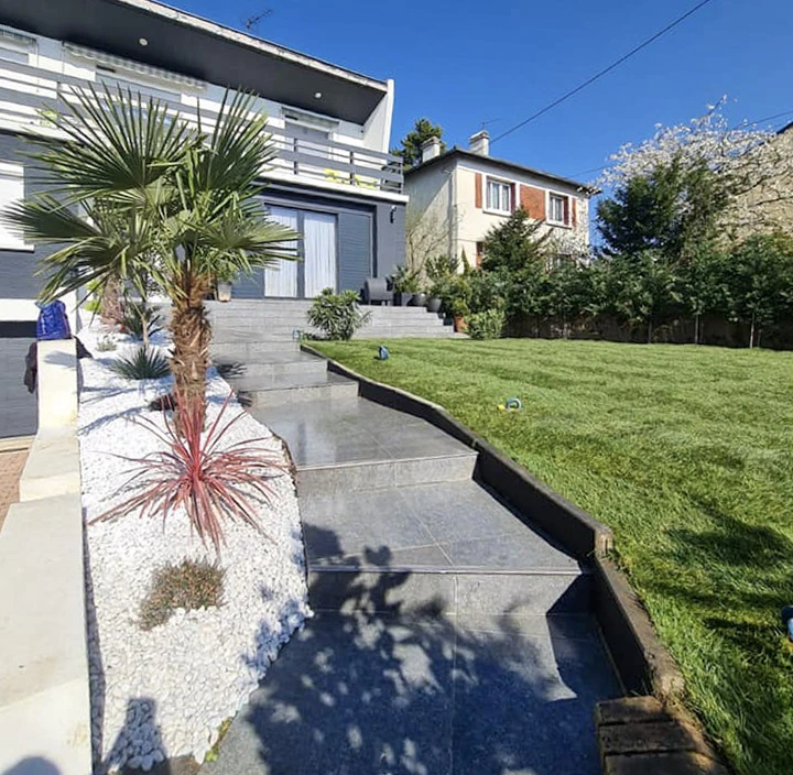 Aménagement paysager extérieur résidentiel avec escalier en béton, muret de soutènement et plantation de palmier